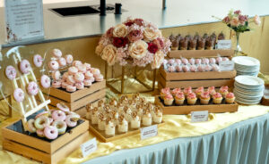 Wedding lunch catering featuring desserts in wooden crates and plates such as bite sized bliss donuts, lotus biscoff in cups, frosty peaks cupcakery, pop-a-delight cakery and pink macaroons by idocatering